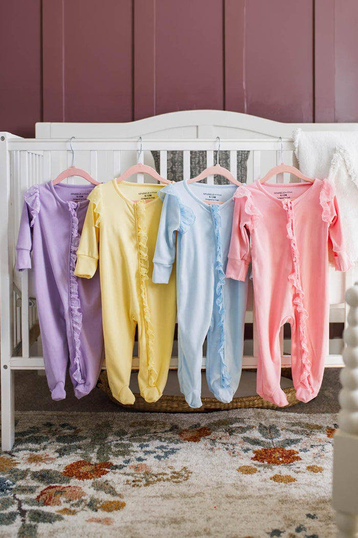 Pastel Ribbed Onesie - Pink / Newborn - Pastel ribbed baby onesies in purple, yellow, blue, and pink with long sleeves and footed bottoms hanging on a white crib.