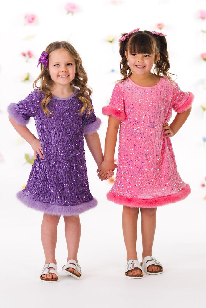Sparkle Plush Sequin Dress - Pink / 6-12 Months - Girls wearing sparkly sequin dresses in purple and pink with ruffled short sleeves and hems, paired with sandals.