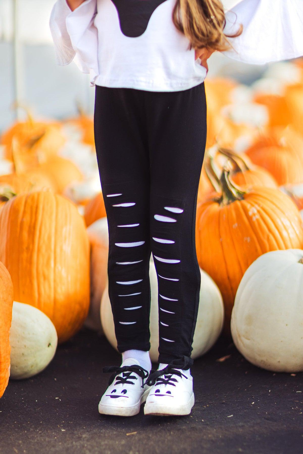 Black & White Ghost Distressed Legging Set - 3XS-6-12 Months - Black leggings with distressed horizontal slits on the front, paired with a white shirt and white sneakers, standing among.