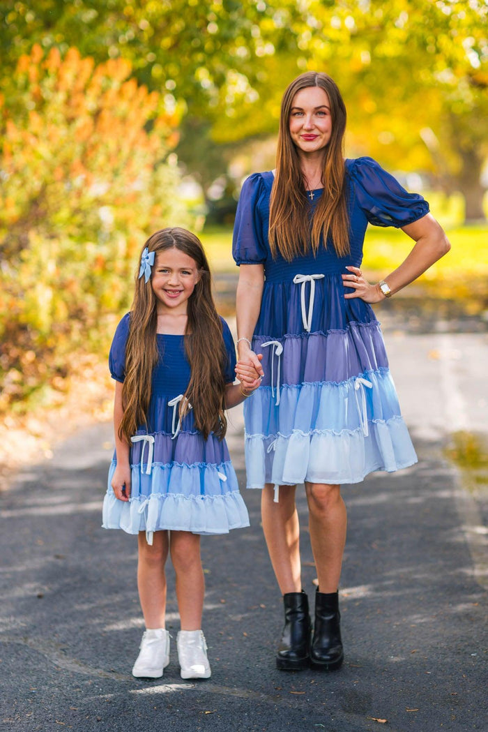 Mom & Me - Blue Ruffle Bow Dress - CHILD-3XS-6-12 Months - Matching blue ruffle bow dresses with puff sleeves and tiered skirt, worn by woman and girl outdoors.