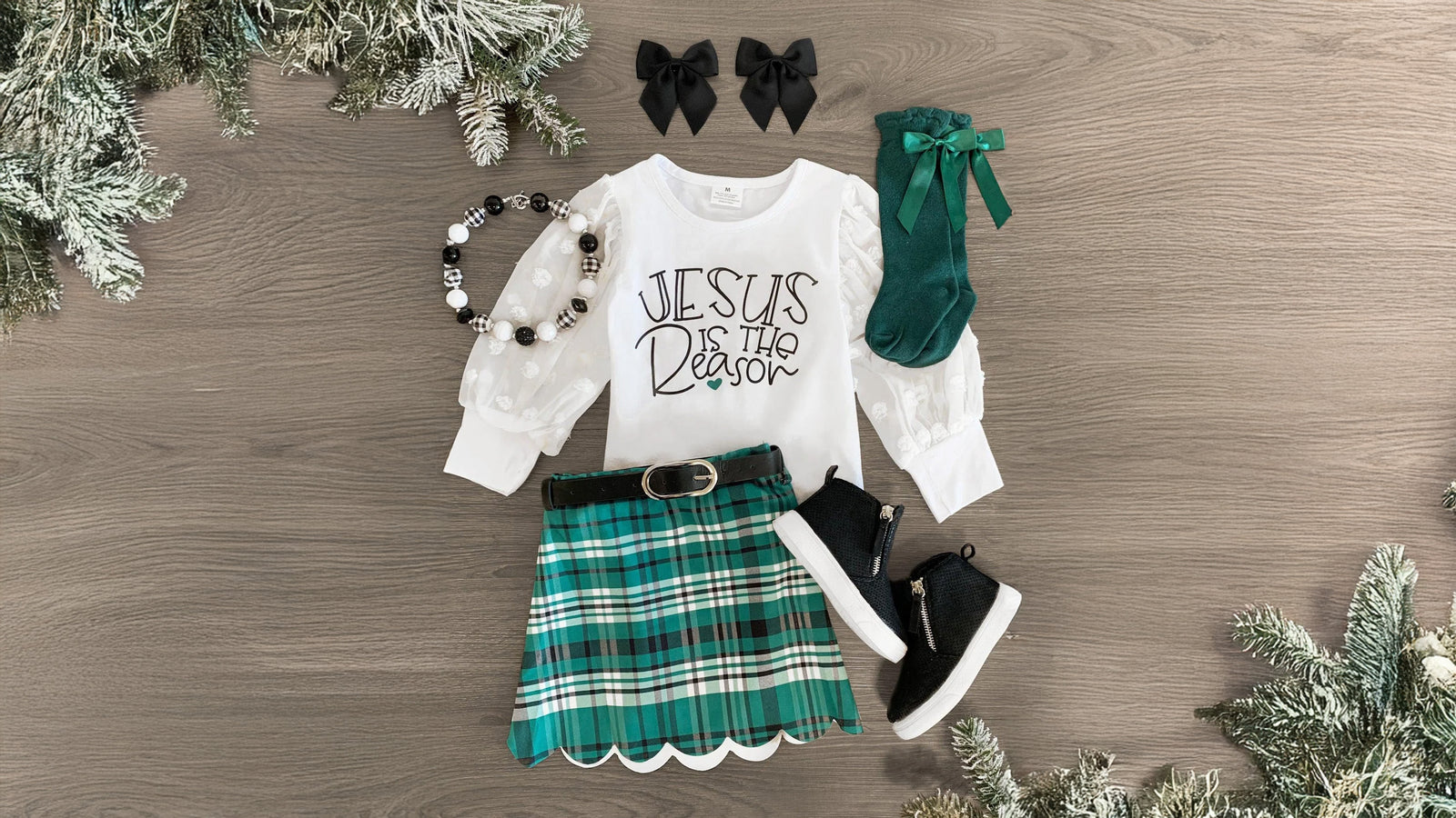 Girls' holiday outfit featuring a long sleeve top with spotted chiffon sleeves and 'Jesus Is The Reason' embossed on the front, paired with a plaid skirt and matching belt. The skirt includes a stretchy waistband for added comfort and easy fit, making it perfect for winter festivities. This set can be styled with bows or booties, creating a festive and versatile holiday look.