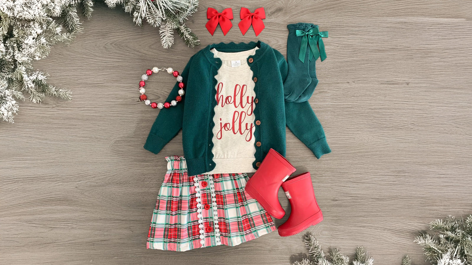 Girls' festive outfit set featuring a cream long sleeve top with 'Holly Jolly' printed across the front, a plaid skirt with a stretchy waistband and decorative buttons, and a cozy green button-up cardigan with long sleeves. Made from ultra-soft, breathable fabric, this set offers comfort and style, perfect for holiday occasions.