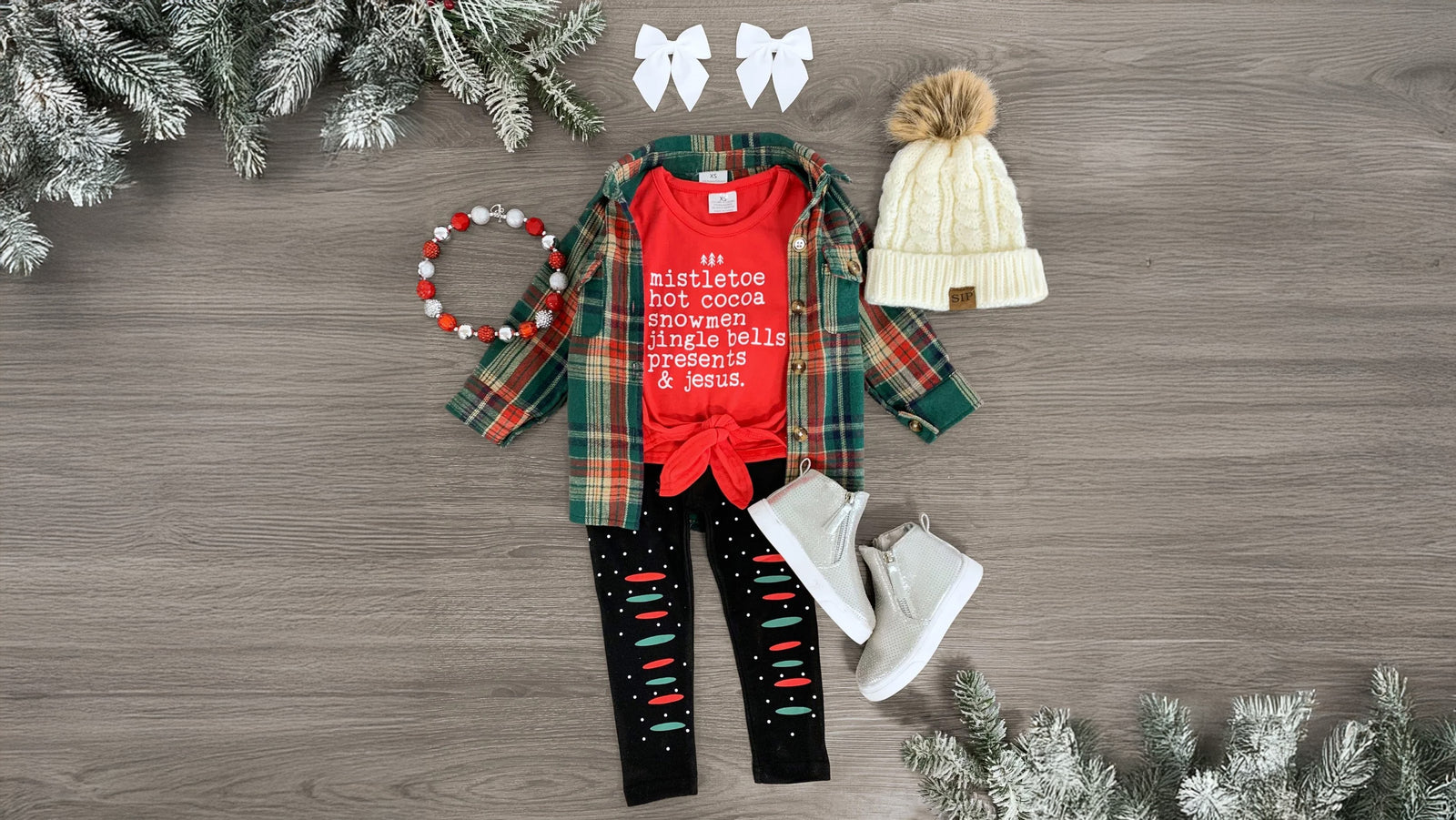 Girls' festive winter outfit set featuring a red short sleeve tie-front top with 'Mistletoe, Hot Cocoa, Snowmen, Jingle Bells, Presents & Jesus' embossed on the front. Paired with faux distressed leggings with a stretchy waistband for comfort and style, this ultra-soft set is perfect for the holiday season. Pair with matching bows or booties to complete the cozy, playful look.