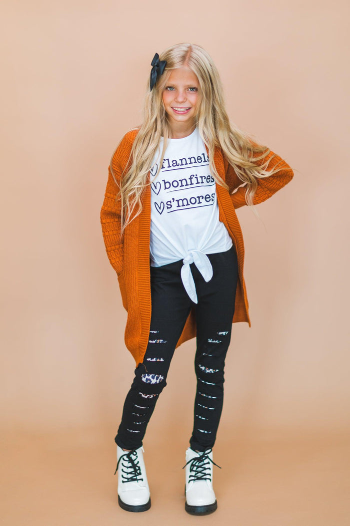 "Flannels, Bonfires, S'mores" Legging Set - 3XS-6-12 Months - Girl wearing white knotted tee with "Flannels bonfires s'mores" text, burnt orange cardigan, black leggings with white text, .