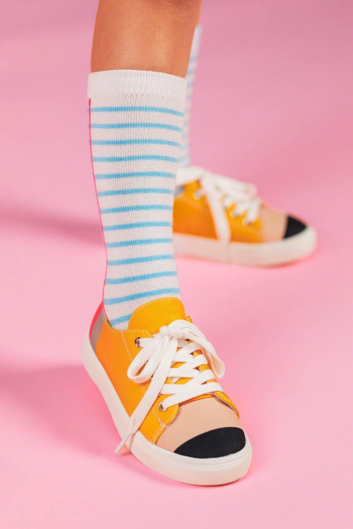 Pencil Sneakers - KIDS-8T - Yellow canvas sneakers with black toe caps and white laces on feet wearing blue-striped white socks against pink background.