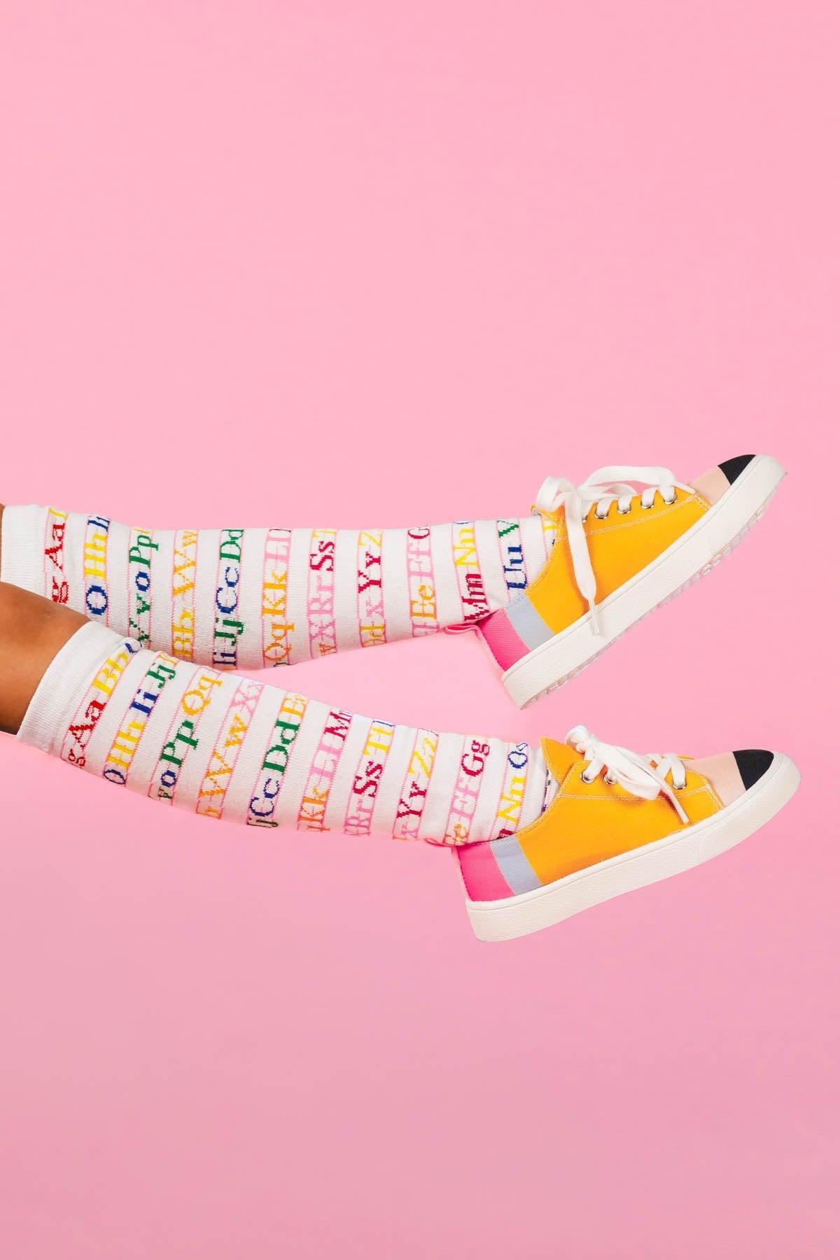 White Alphabet Knee High Socks - Default Title - White knee-high socks with colorful alphabet letters paired with yellow and white canvas sneakers on pink background.