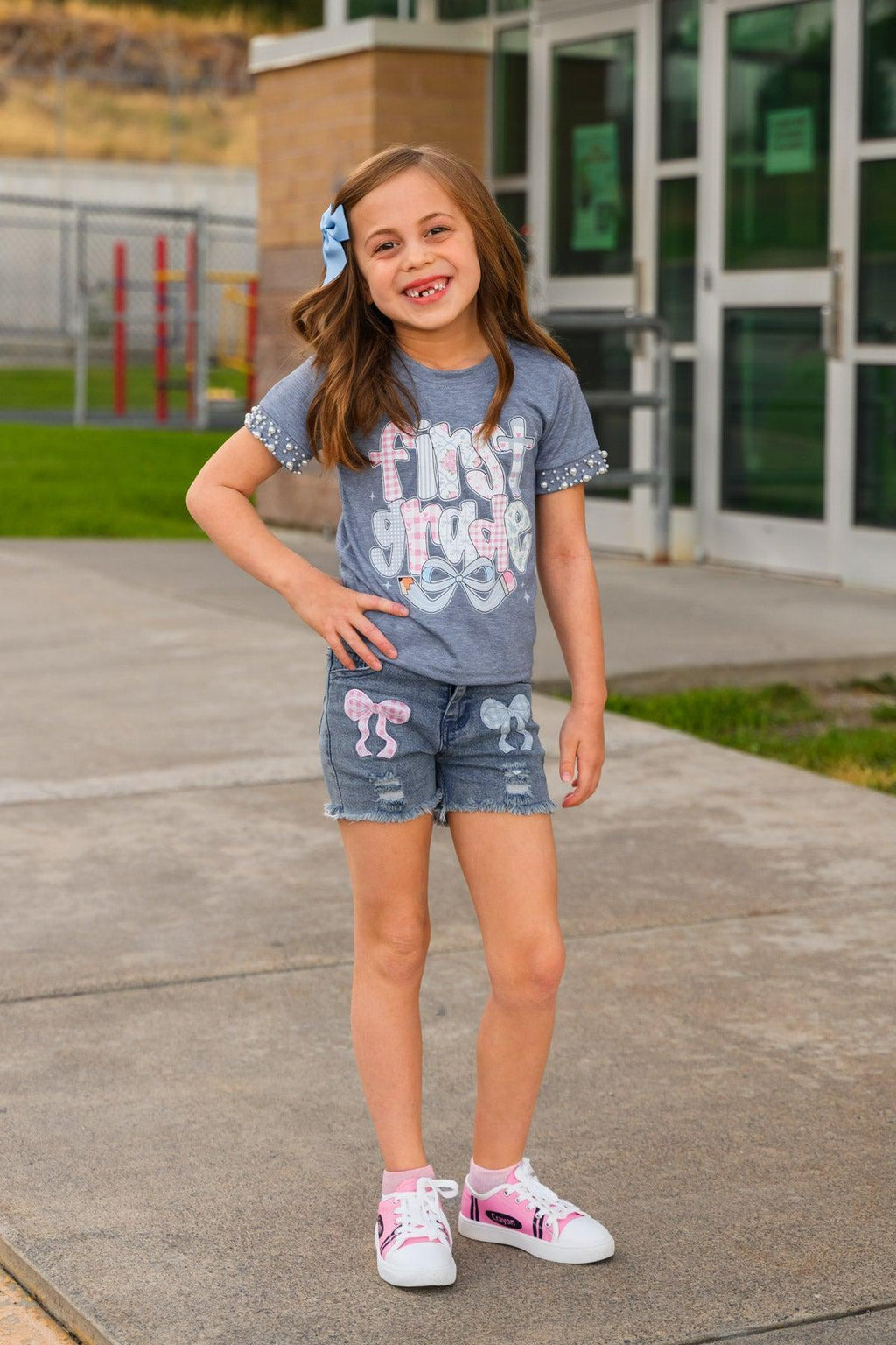 "Pre-K - Sixth Grade" Plaid Bow Denim Short Set - PRE-K / 2T - Blue denim shorts and plaid bow set with a gray graphic t-shirt and pink-accented sneakers worn by a young girl.