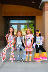 Pink School Supplies Jumpsuit - 3T - Pink jumpsuit with colorful school supply prints and ruffled sleeves on girl standing outside.
