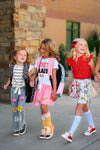 Notebook Bow Flare Denim Pant Set - 3T - Three young girls wearing colorful patterned outfits, including denim jeans with floral embroidery, a pink skirt with.