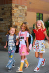 "Pre-K - 6th Grade" Pink Pencil Tutu Skirt Set - PRE-K / 2T - Three young girls wearing colorful casual outfits with one in a pink tutu skirt, smiling outdoors.