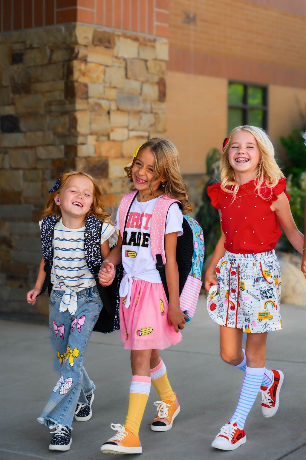 "Pre-K - 6th Grade" Pink Pencil Tutu Skirt Set - PRE-K / 2T - Three young girls wearing colorful casual outfits with one in a pink tutu skirt, smiling outdoors.