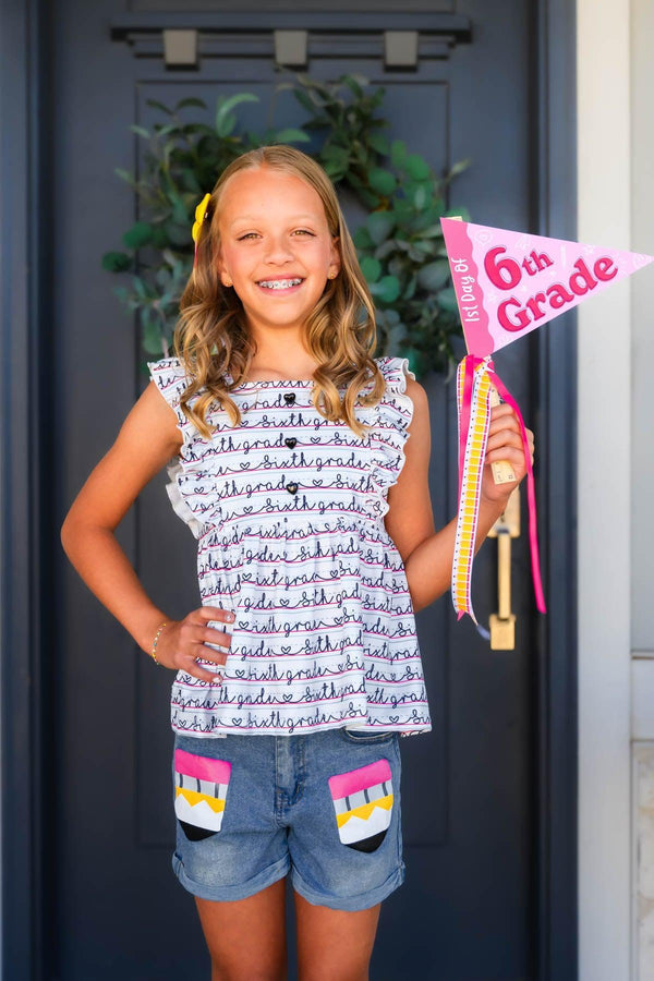 "Pre-K - Sixth Grade" Notebook Denim Short Set - PRE-K / 2T - Girl wearing white sleeveless top with navy handwritten script and denim shorts with colorful patch pockets holding 6th.