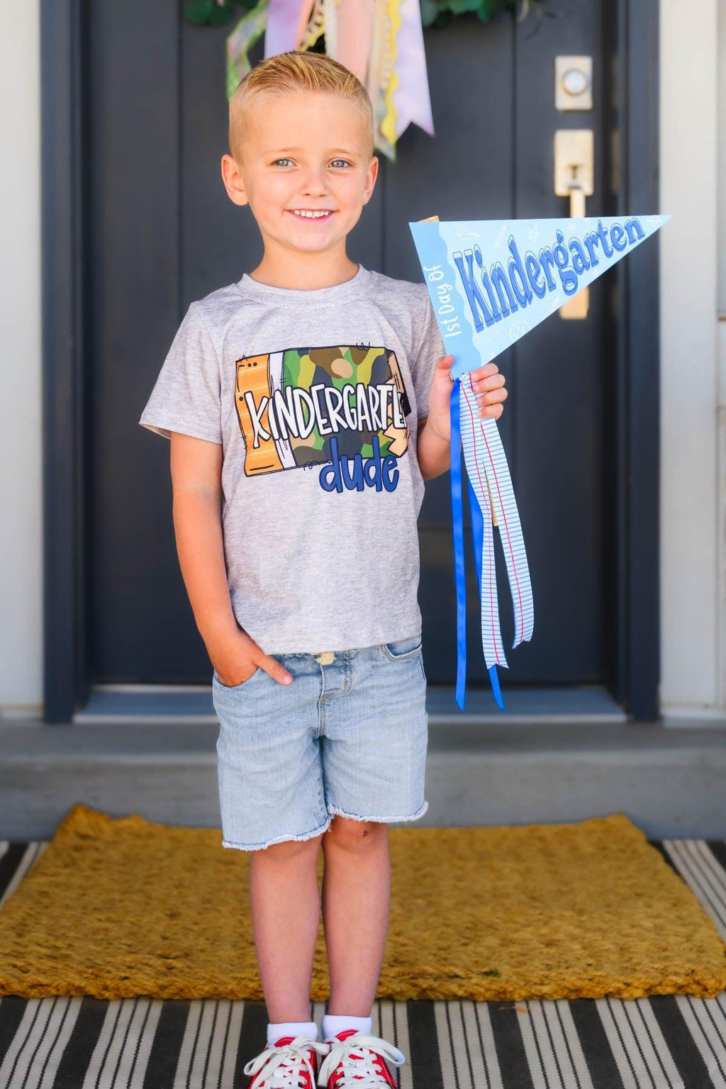 "Preschool - 5th Grade Dude" Camo Pencil Top - PRESCHOOL / 2T - Gray camo pencil top with "Preschool - 5th Grade Dude" text worn by boy in light blue shorts holding kindergarten flag.