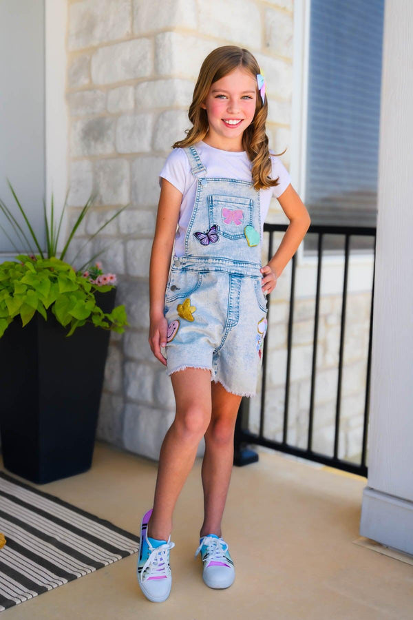 Summer Patches Denim Overalls - 6-12 Months - Light-wash denim overall shorts with colorful summer-themed patches worn over a white t-shirt, paired with white sneakers.