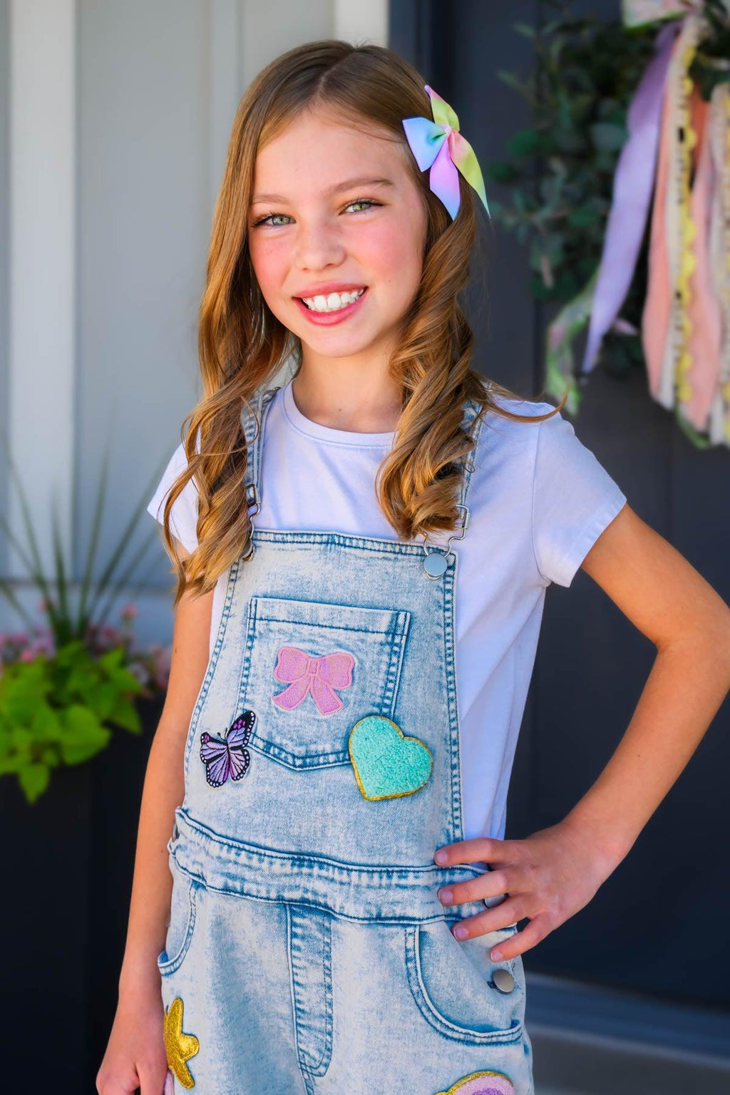 Summer Patches Denim Overalls - 6-12 Months - Light blue denim overalls with colorful butterfly, heart, and bow patches worn over white t-shirt by smiling girl with bow.