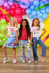"Be Kind" Crayon Skirt Set - 3T - Girls wearing colorful casual outfits; one in blue skirt with "Be Kind" text, one in red top and light jeans with patches,.