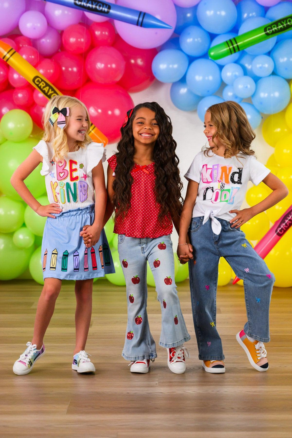 "Kind Is Cool" Denim Pant Set - 3T - Girls wearing colorful casual outfits with graphic tees and denim pants, standing against a bright balloon backdrop.