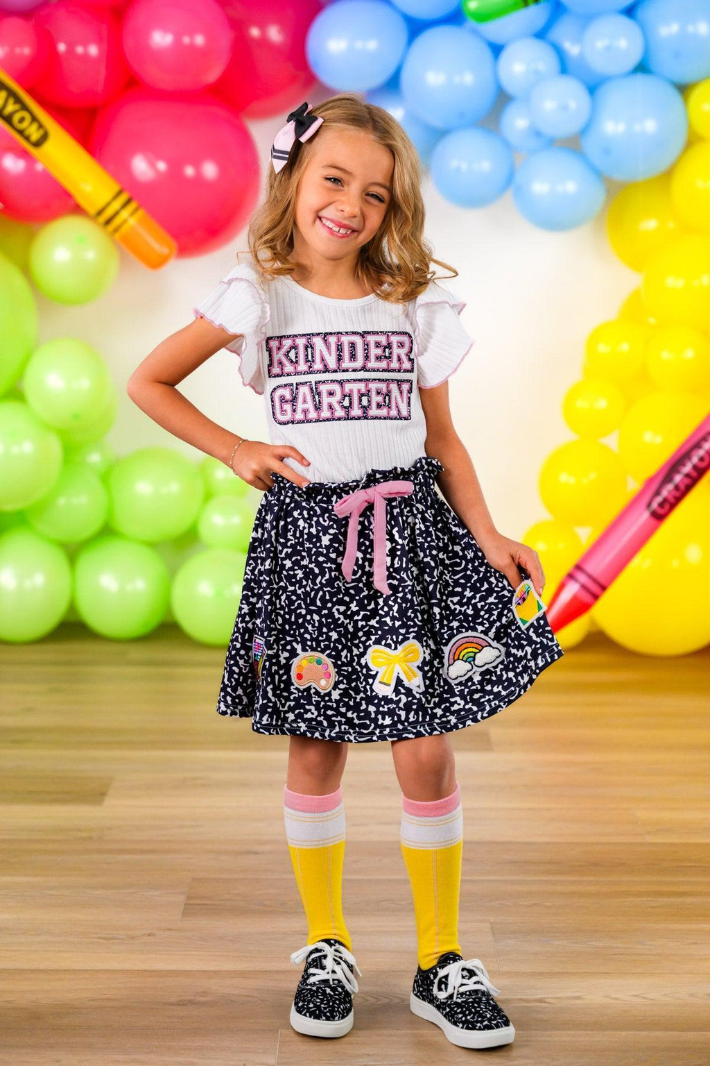 "Pre-K - Sixth Grade" Notebook Skirt Set - PRE-K / 2T - White short-sleeve shirt with "Kinder Graven" text paired with black skirt featuring multicolored cartoon patches and pink.