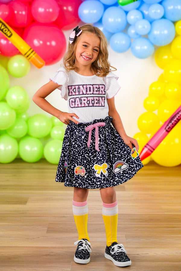 "Pre-K - Sixth Grade" Notebook Skirt Set - PRE-K / 2T - White short-sleeve shirt with "Kinder Graven" text paired with black skirt featuring multicolored cartoon patches and pink.