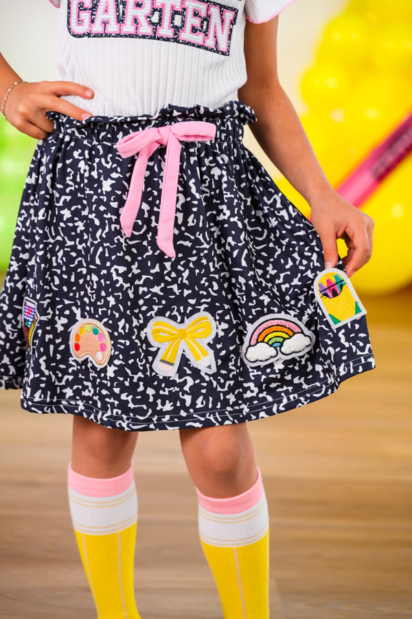 "Pre-K - Sixth Grade" Notebook Skirt Set - PRE-K / 2T - Black gathered skirt with colorful patches and a pink drawstring waistband worn with knee-high white socks with pink stripes.