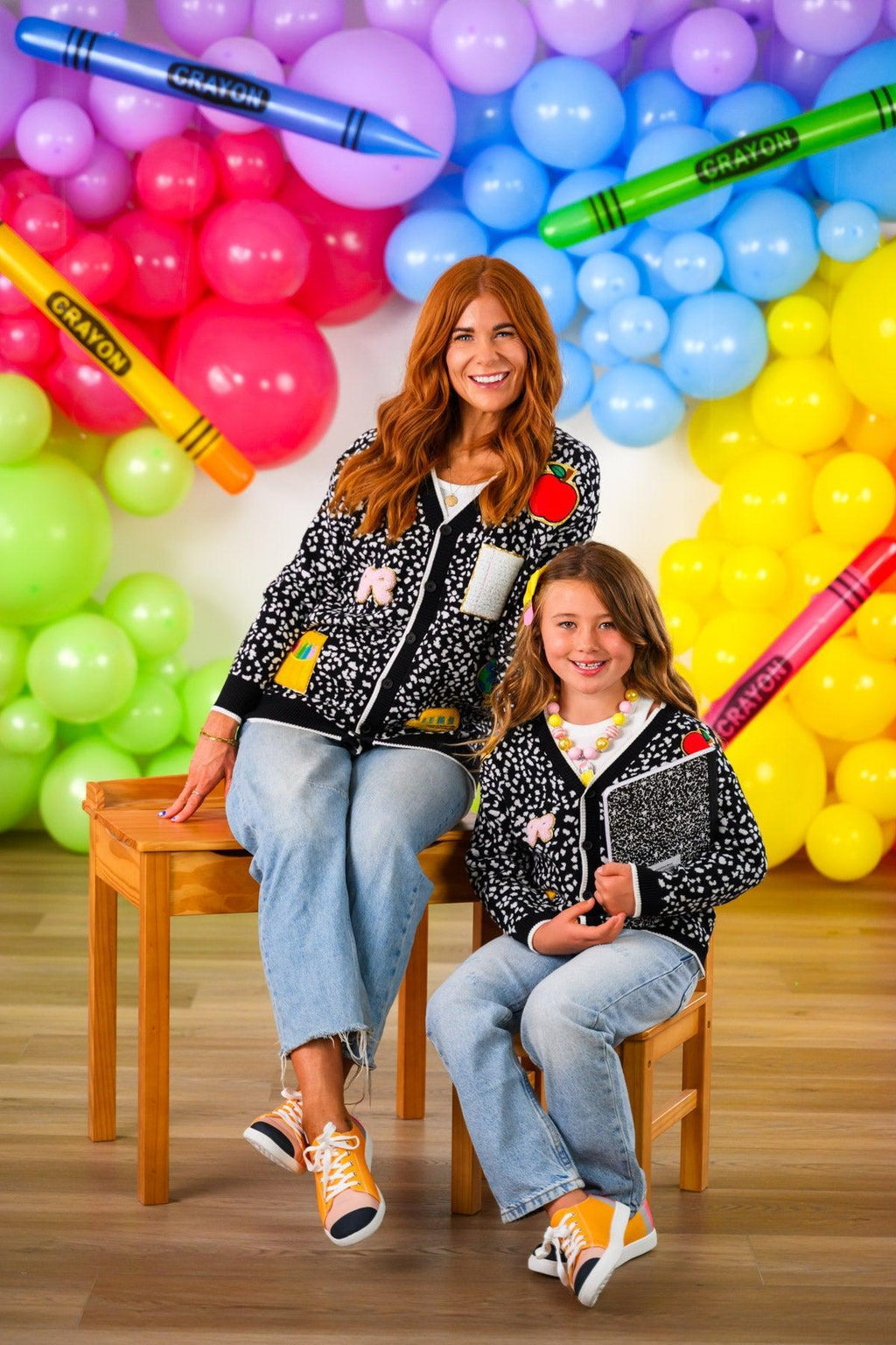 Mom & Me - Composition Sweater Cardigan - CHILD-3T - Black knit sweater cardigans with white and yellow graphic details worn by woman and girl sitting on wooden bench.