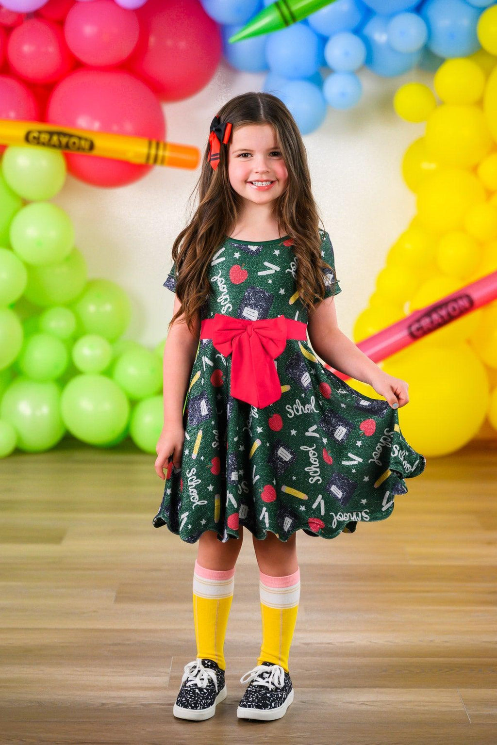 Green Glitter School Supplies Dress - 3T - Green dress with school supply print, glitter accents, red bow waist, and short sleeves on girl.