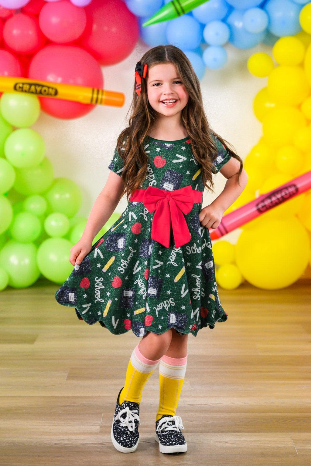 Green Glitter School Supplies Dress - 3T - Green knee-length dress with glittery school supply patterns, puffed sleeves, and a large red bow at the waist.