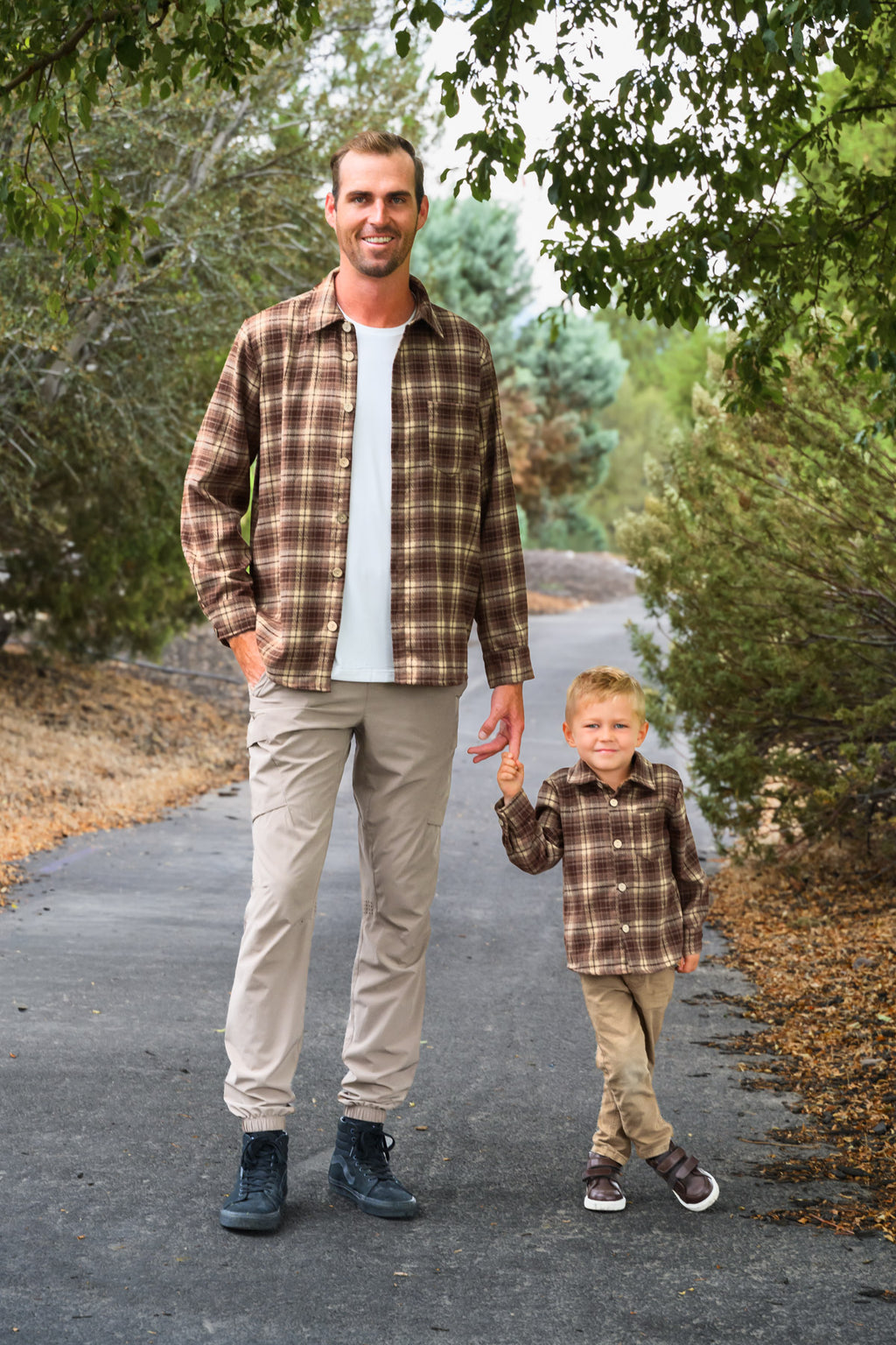 Family Brown Dress & Flannel - GIRL-6-12 Months-FAMILY - Men's and toddler's brown plaid flannel shirts paired with beige pants on a paved outdoor path.