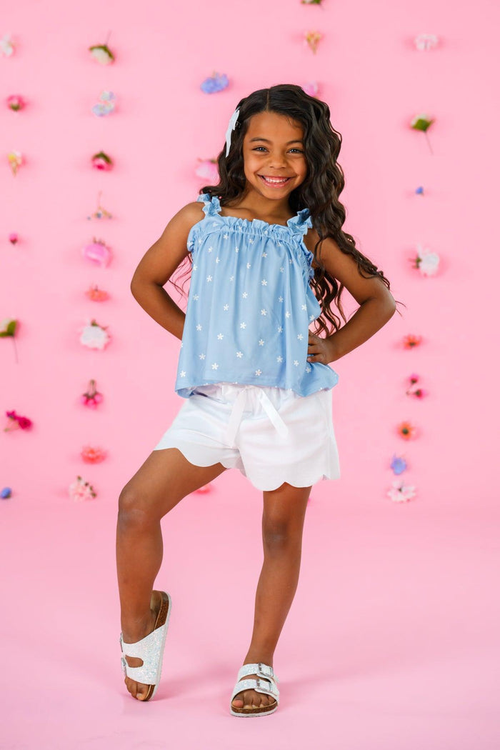 Blue & White Flower Short Set - 6-12 Months - Blue sleeveless top with white floral print and ruffled neckline paired with white scalloped shorts on a smiling girl.