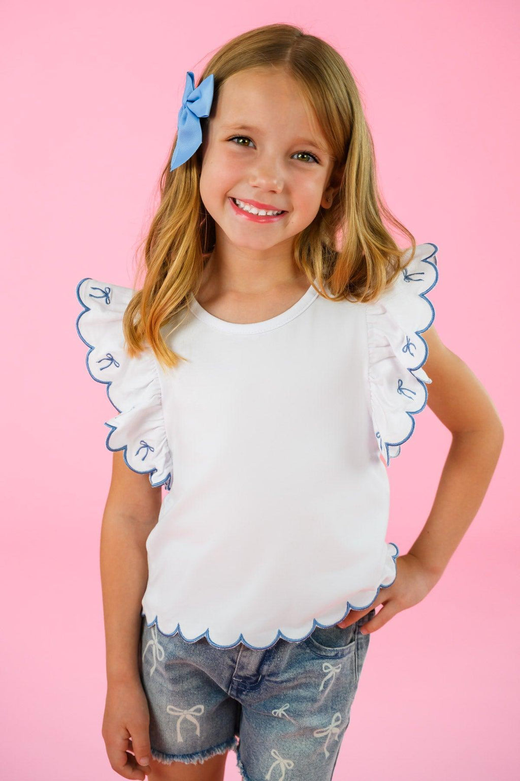 White & Blue Bow Denim Short Set - 6-12 Months - White scalloped sleeve top with blue trim paired with distressed blue denim shorts and a large blue bow hair accessory.