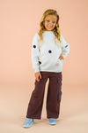 Knit Flower Burgundy Denim Pant Set - 6-12 Months - Girl wearing a white knit sweater with burgundy flower accents paired with loose burgundy denim cargo pants.