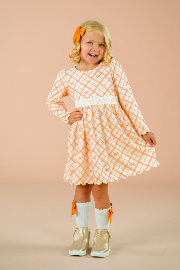 Orange Plaid Bow Dress - 6-12 Months - Orange and white plaid long-sleeve dress with a large bow detail and gathered waist, worn by a smiling child with matching.