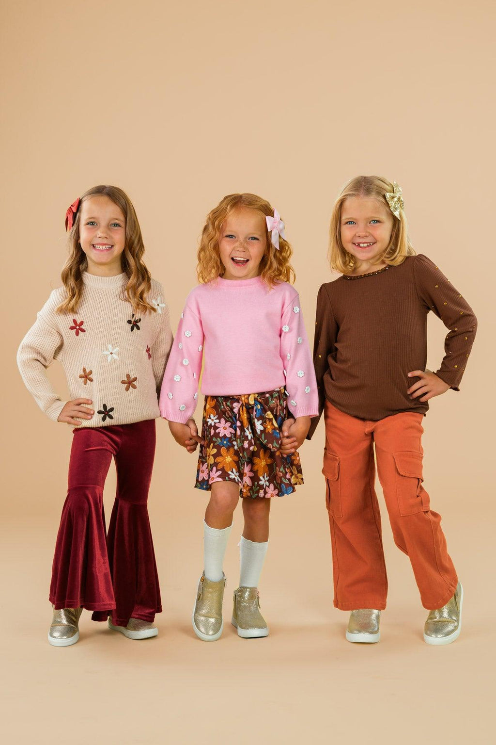 Pink & Brown Floral Skirt Set - 6-12 Months - Left girl in cream sweater with star patterns and burgundy flared pants, center girl in pink long-sleeve top with floral.