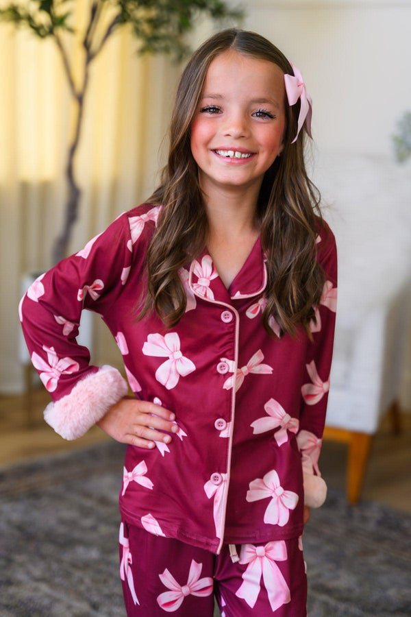 Mom & Me - Fuzzy Pink Bow Pajamas - CHILD-6-12 Months - Burgundy pajama set with pink fuzzy bows, button-up top with pink fuzzy cuffs, worn by smiling girl with pink hair bow.