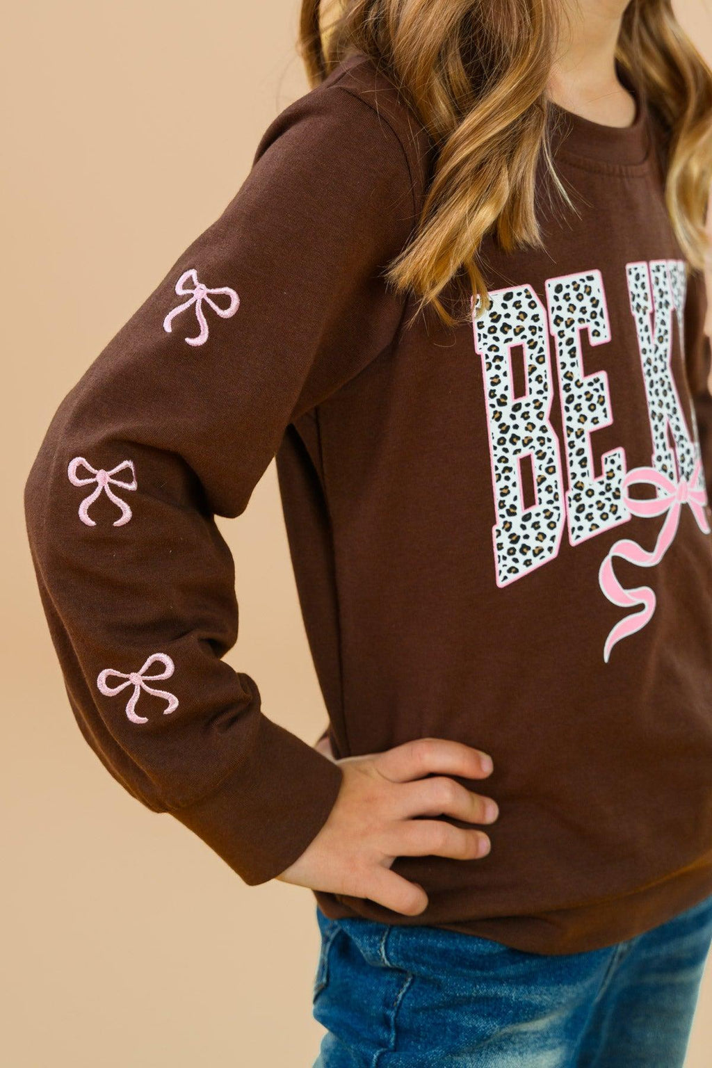 "Be Kind" Cheetah Denim Bell Bottom Set - 6-12 Months - Brown long-sleeve sweatshirt with "BE KIND" cheetah print lettering and pink bow accents on sleeves and front.