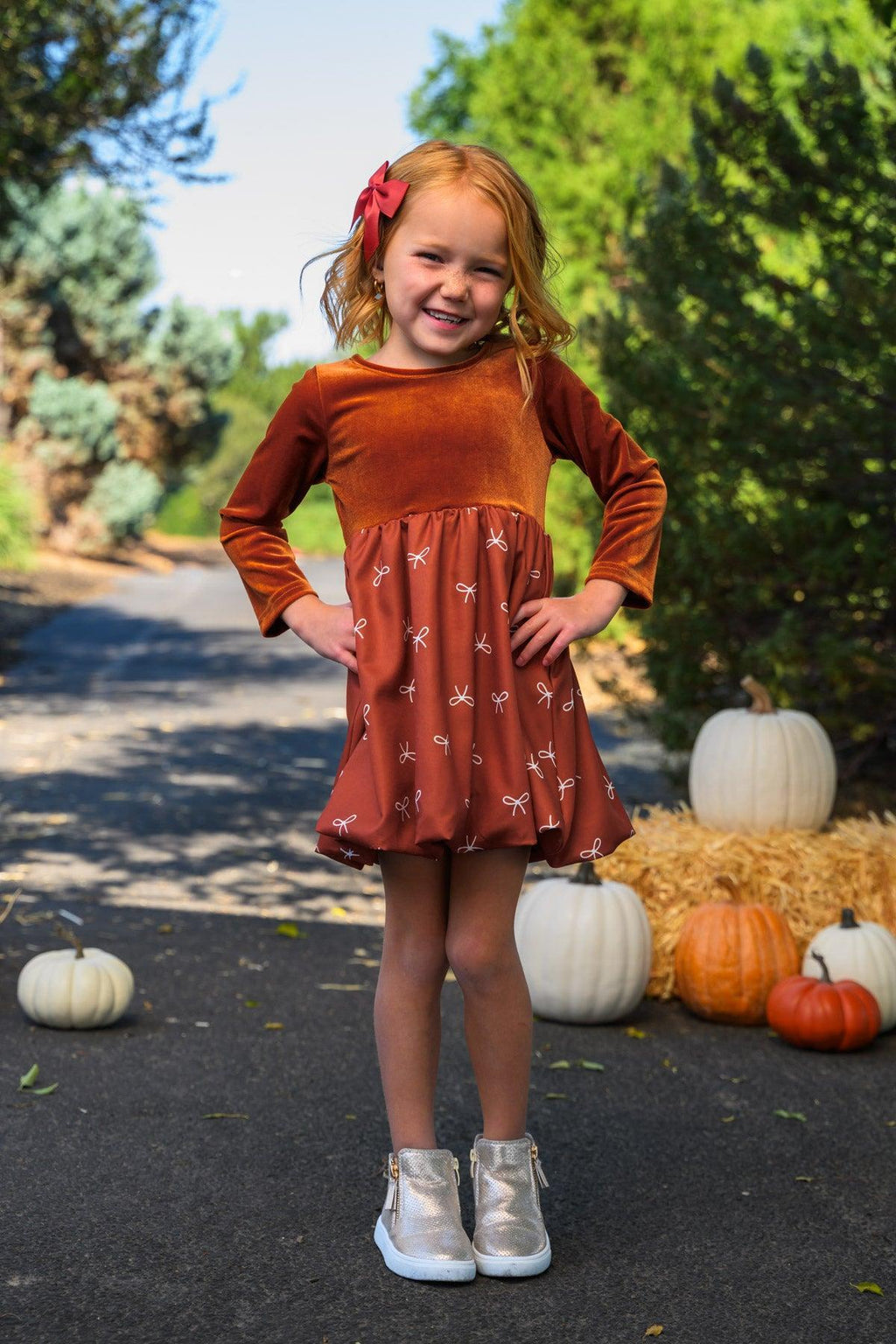 Rust Velvet Bow Dress - 6-12 Months - Rust velvet long-sleeve dress with bow detail and printed skirt panel worn by child outdoors.