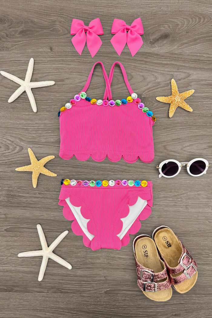 Pink Gemstone Bikini - 6-12 Months - Pink scalloped bikini set with multicolored pom-poms, matching pink bow hair clips, white sunglasses, and brown toddler.
