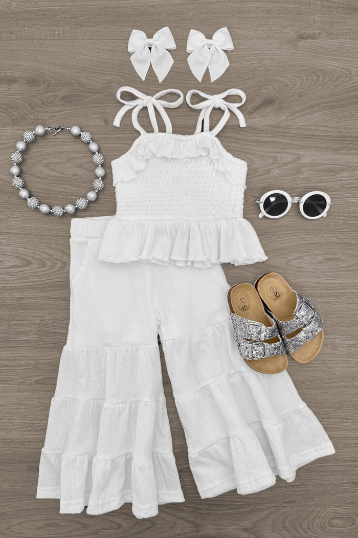 White Flowy Ruffle Flare Pant Set - 6-12 Months - White sleeveless ruffle crop top and flare pants set with matching bows, sandals, sunglasses, and beaded necklace.