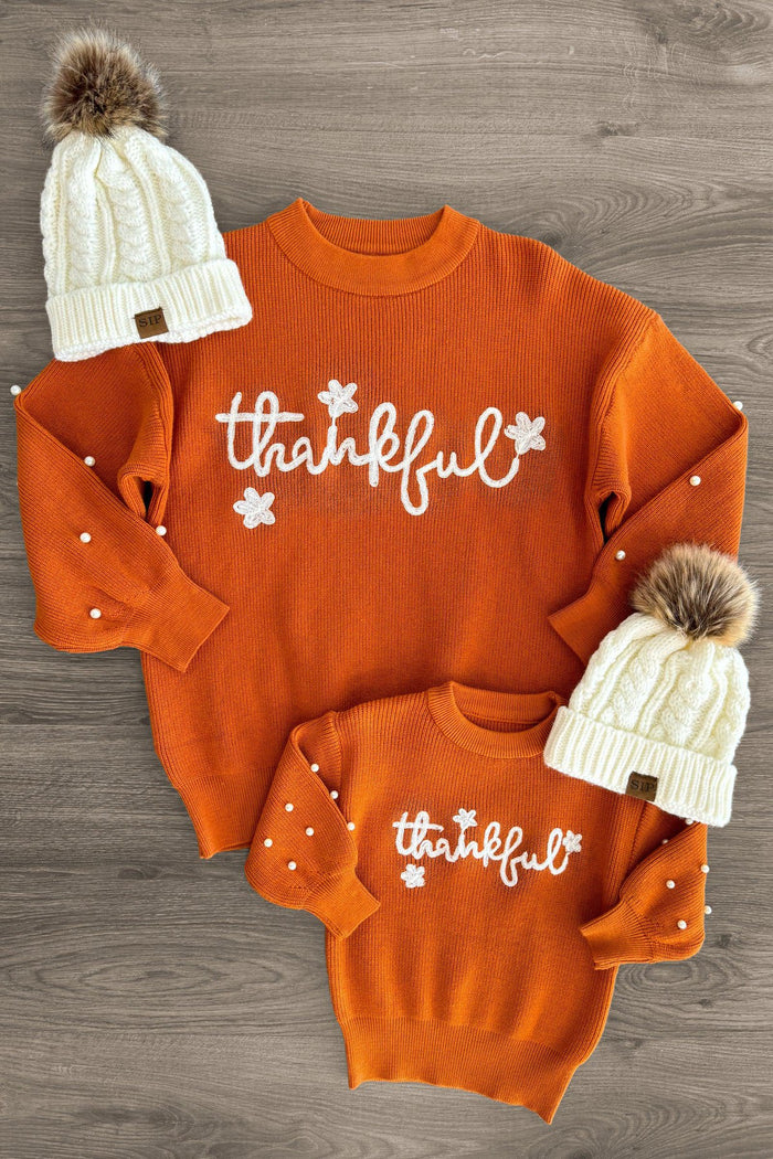 Mom & Me - "Thankful" Orange Pearl Sweater - CHILD-3XS-6-12 Months - Orange knit sweaters with white "thankful" text and floral details, paired with cream cable-knit beanies with brown pom-poms.