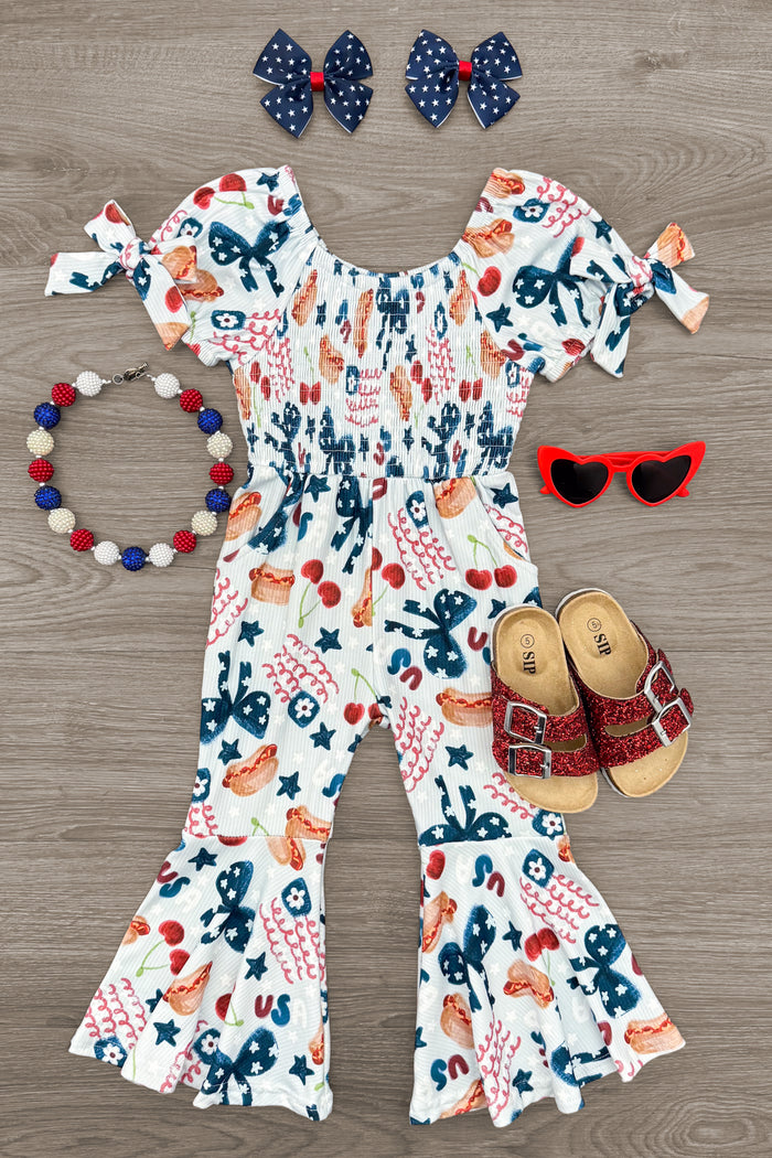 USA Bell Bottom Jumpsuit - 6-12 Months - White bell bottom jumpsuit with colorful floral and cactus print, puff sleeves, and tie cuffs, paired with red sunglasses,.