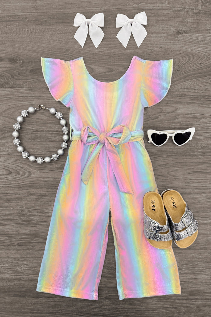 Holographic Glitter Jumpsuit - 6-12 Months - Rainbow holographic glitter jumpsuit with flutter sleeves and front tie detail, paired with white bow clips, heart-shaped.