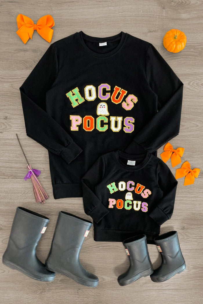 Mom & Me - "Hocus Pocus" Black Chenille Patch Top - CHILD-3XS-6-12 Months - Black chenille patch tops with colorful "Hocus Pocus" text for mom and child with gray boots and orange hair bows nearby.