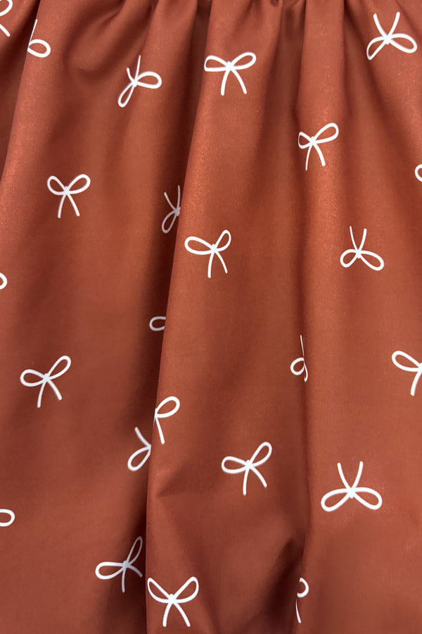 Rust Velvet Bow Dress - 6-12 Months - Rust-colored velvet fabric with small white bow patterns scattered across the surface.