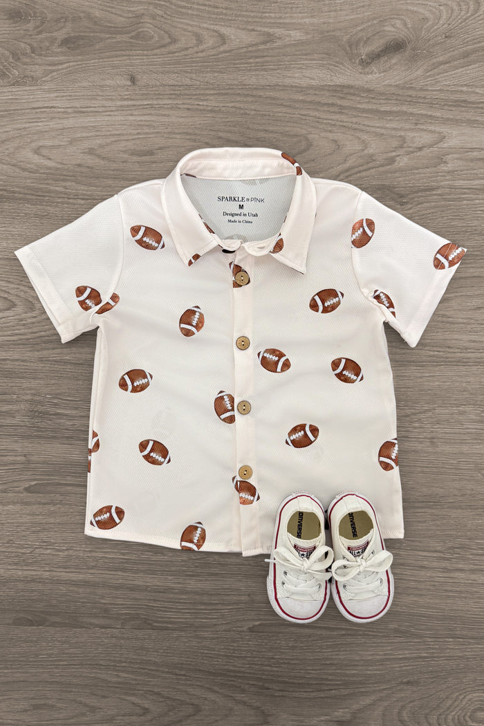 Football Button Down Top - 3XS-6-12 Months - Cream short-sleeve button-down shirt with all-over brown football print, paired with white baby sneakers.
