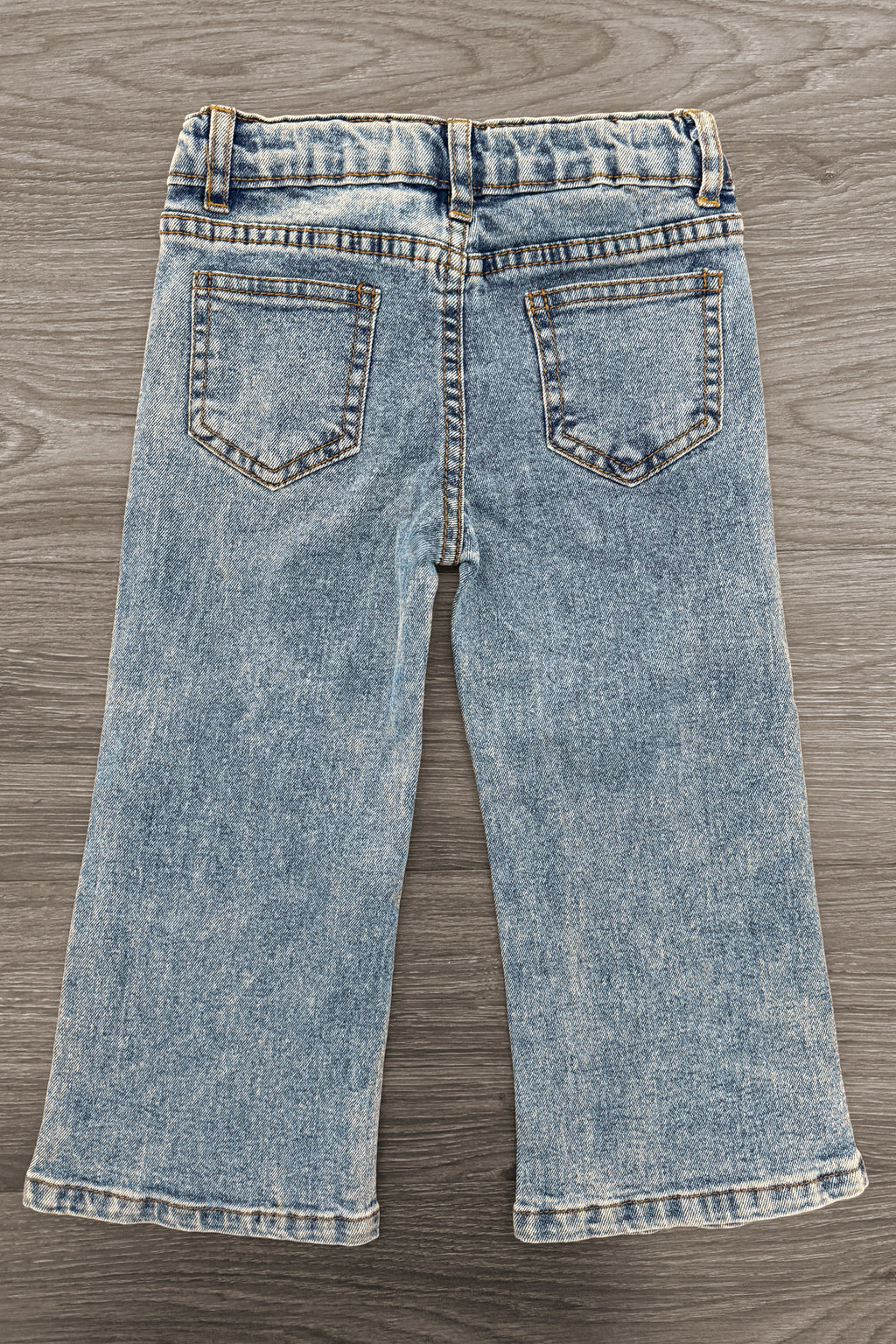 Gemstone Denim Pants - 6-12 Months - Light blue denim pants with a slightly flared leg and two back pockets featuring gemstone embellishments on a wooden floor.