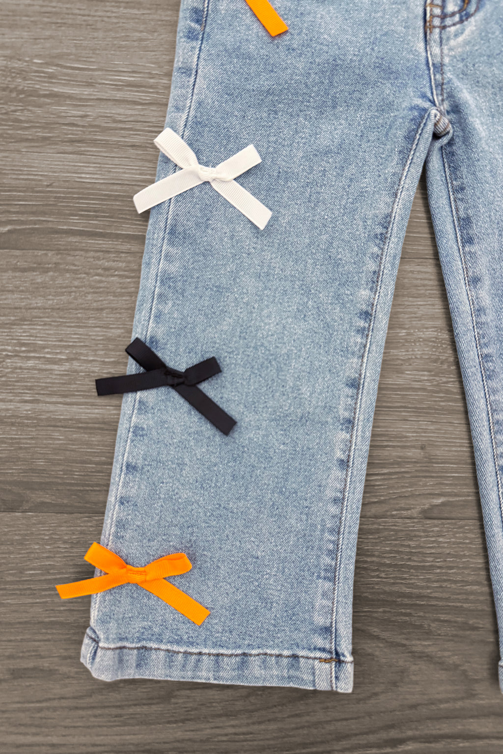 "Spooky Season" Bow Denim Pant Set - 6-12 Months - Light blue denim pants with white, black, and orange bows vertically aligned on the pant leg.