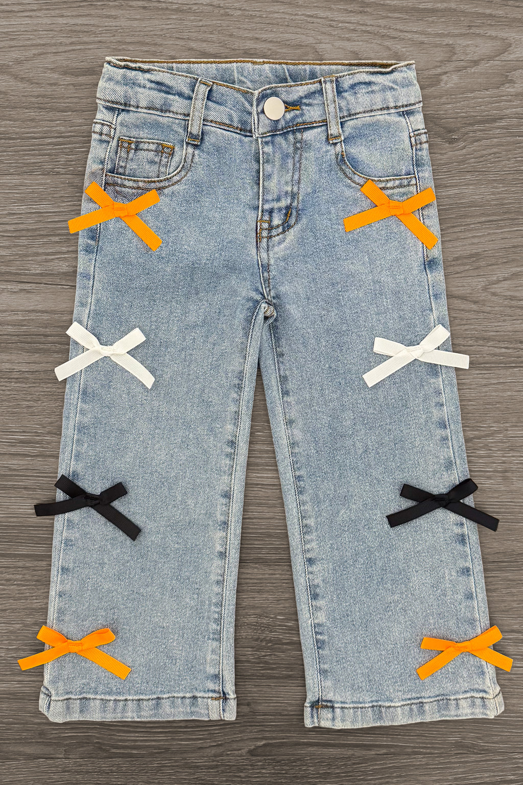 "Spooky Season" Bow Denim Pant Set - 6-12 Months - Light blue denim pants with decorative orange, white, and black bow accents on front legs.