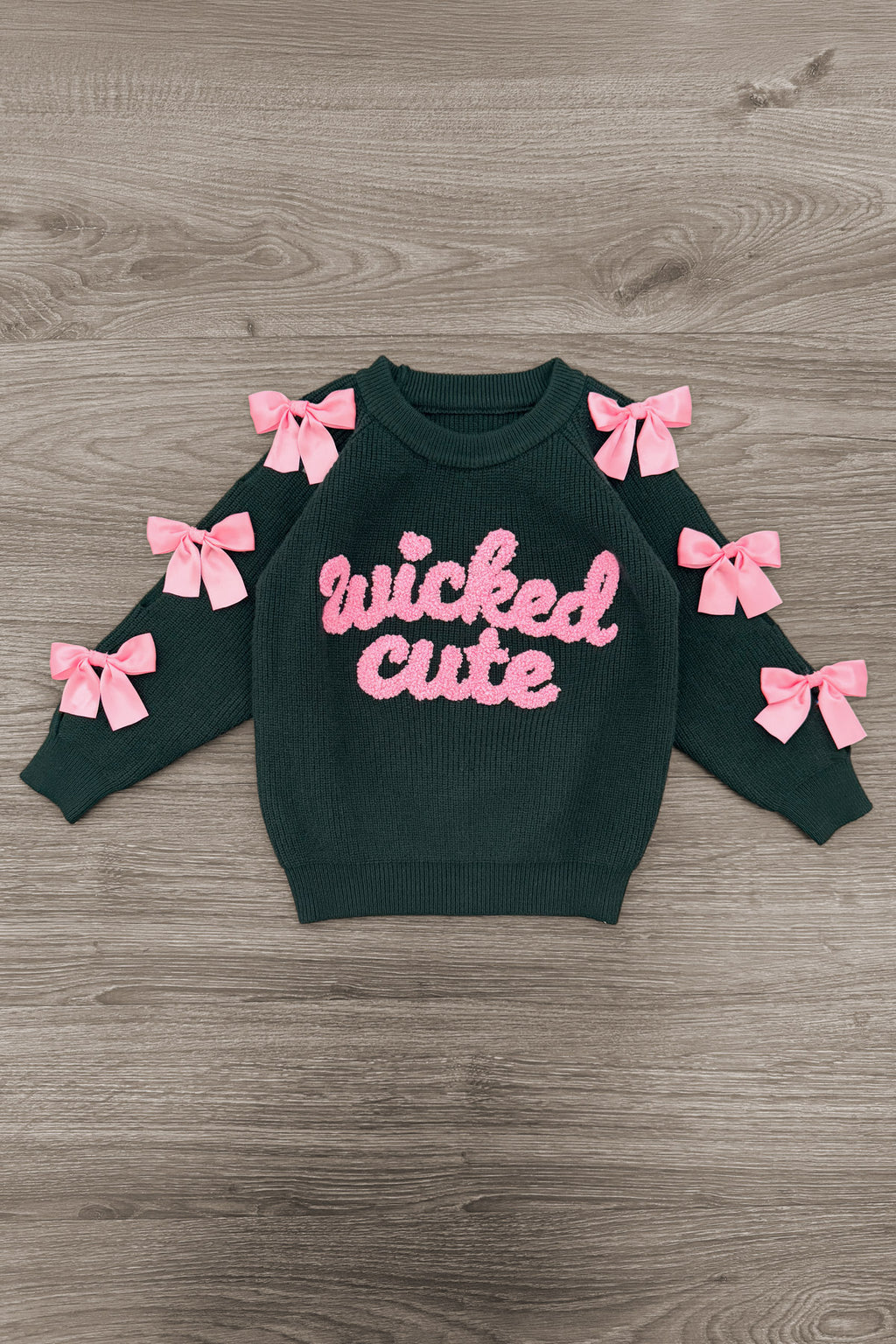 "Wicked Cute" Denim Flare Set - 6-12 Months - Black long-sleeve sweatshirt with pink "wicked cute" text and pink bows on sleeves, laid flat on wood floor.