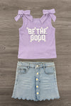 Flat lay of the "Be The Good" Daisy Denim Skirt Set with a lavender bow-strap top and light-wash denim skirt with daisy buttons and scalloped hem.