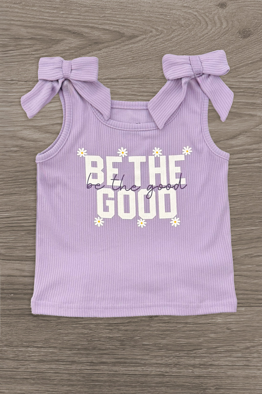 "Be The Good" Daisy Denim Skirt Set - 6-12 Months - Light purple sleeveless top with bow ties on shoulders and "Be The Good" text with daisies in white and yellow.